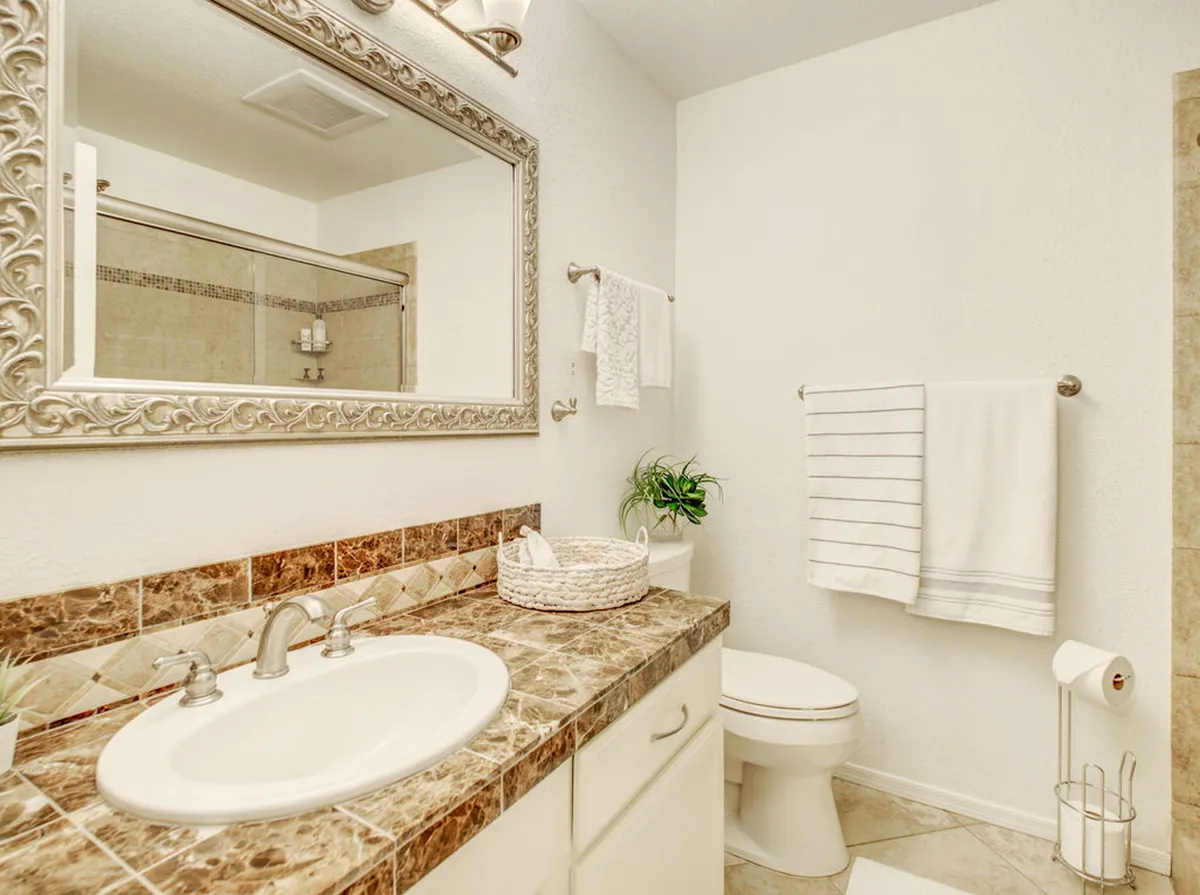 A serene bathroom with a marble countertop, dual sinks, a large framed mirror, and neatly arranged towels. The muted tones and elegant finishes set a tranquil, sophisticated mood ideal for self-care and unwinding.
