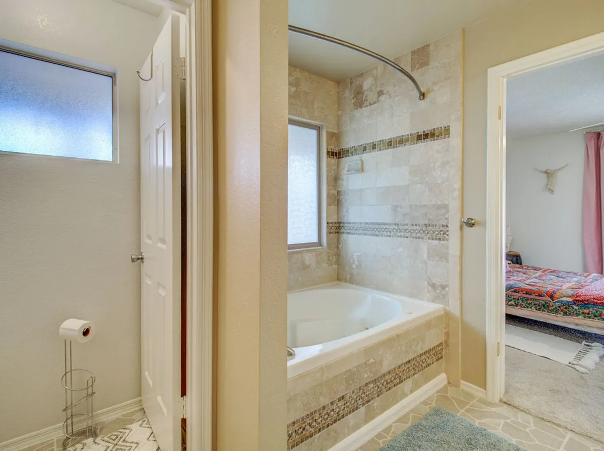 A spa-inspired bathroom showcasing a standalone bathtub, a walk-in shower area with decorative tiles, and a doorway that leads directly to a bedroom. The space exudes a peaceful, rejuvenating mood, with high-end finishes and a clean, organized layout.