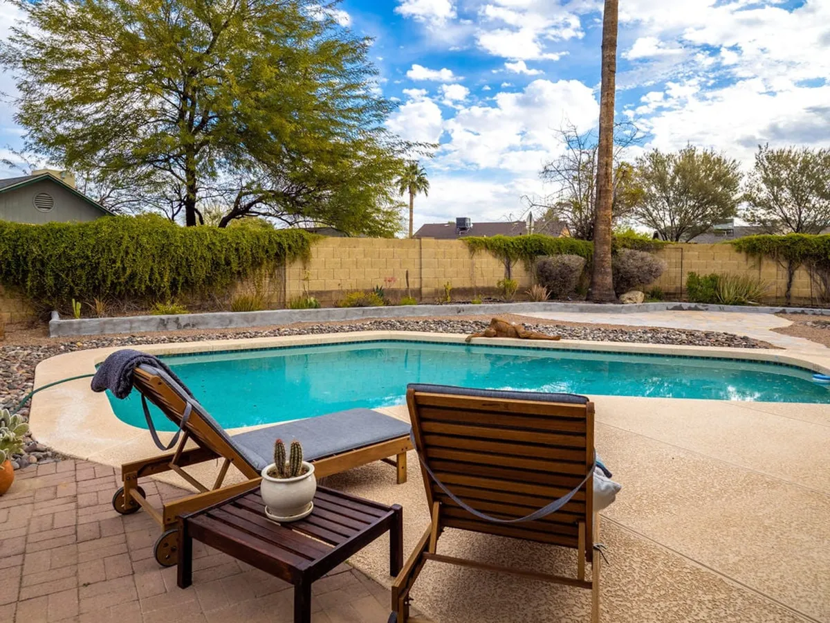 A serene backyard setting at sunset, featuring a sparkling swimming pool surrounded by lounge chairs and a beautifully landscaped garden. The area is set up perfectly for relaxation or entertaining guests, with a tranquil atmosphere highlighted by the warm glow of the evening light.
