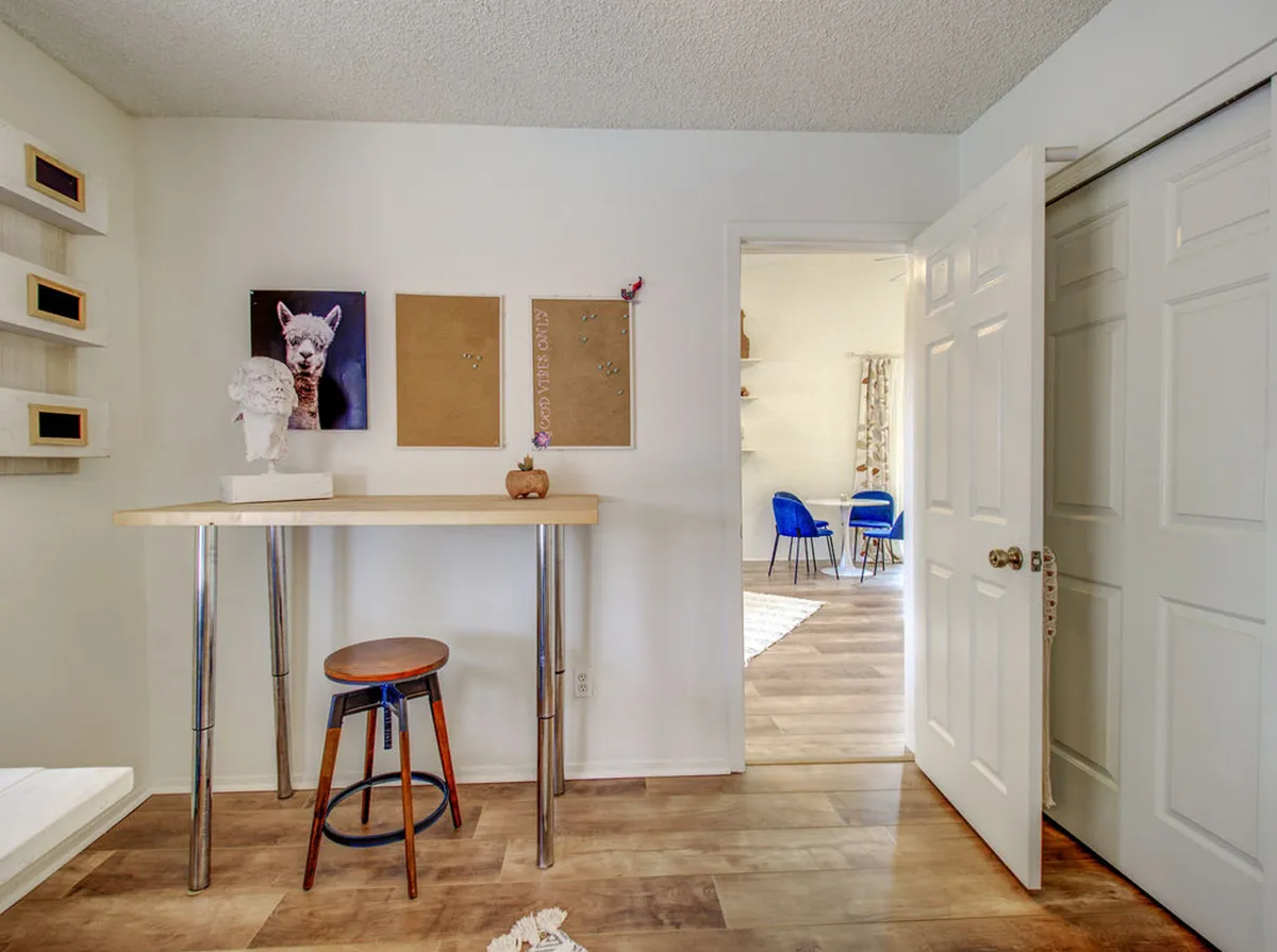 A creative, inviting room with a modern tall table and stool, bright artwork of an alpaca, cork boards for notes or artwork display, and a doorway leading to another space. The setup encourages both productivity and creativity, with plenty of surface area for working or pursuing projects.