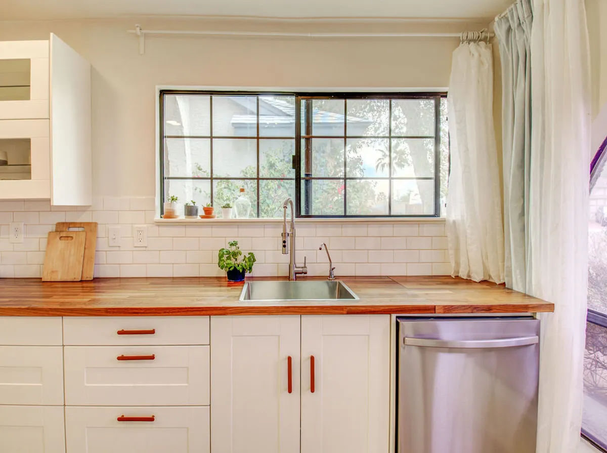 A cozy view of a kitchen sink under a window, with wooden countertops and soft lighting, setting a warm, intimate mood. The space balances practicality and comfort, encouraging moments of togetherness during meal preparation.