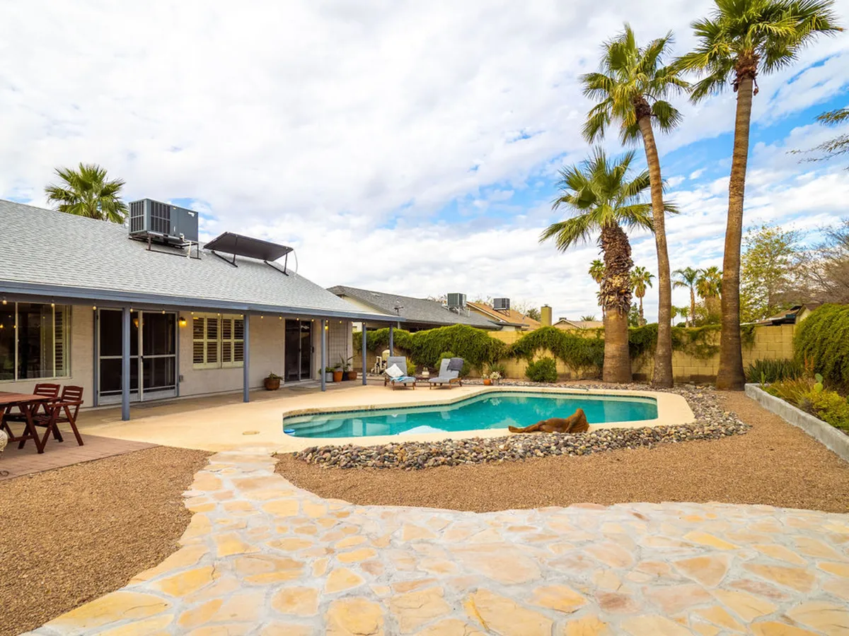 A vibrant exterior view of a swimming pool framed by tall palm trees, a stylish outdoor seating area, and a stone pathway. The setting feels inviting and tranquil, with the space designed for both sunbathing and social gatherings, especially under the golden light of sunset.