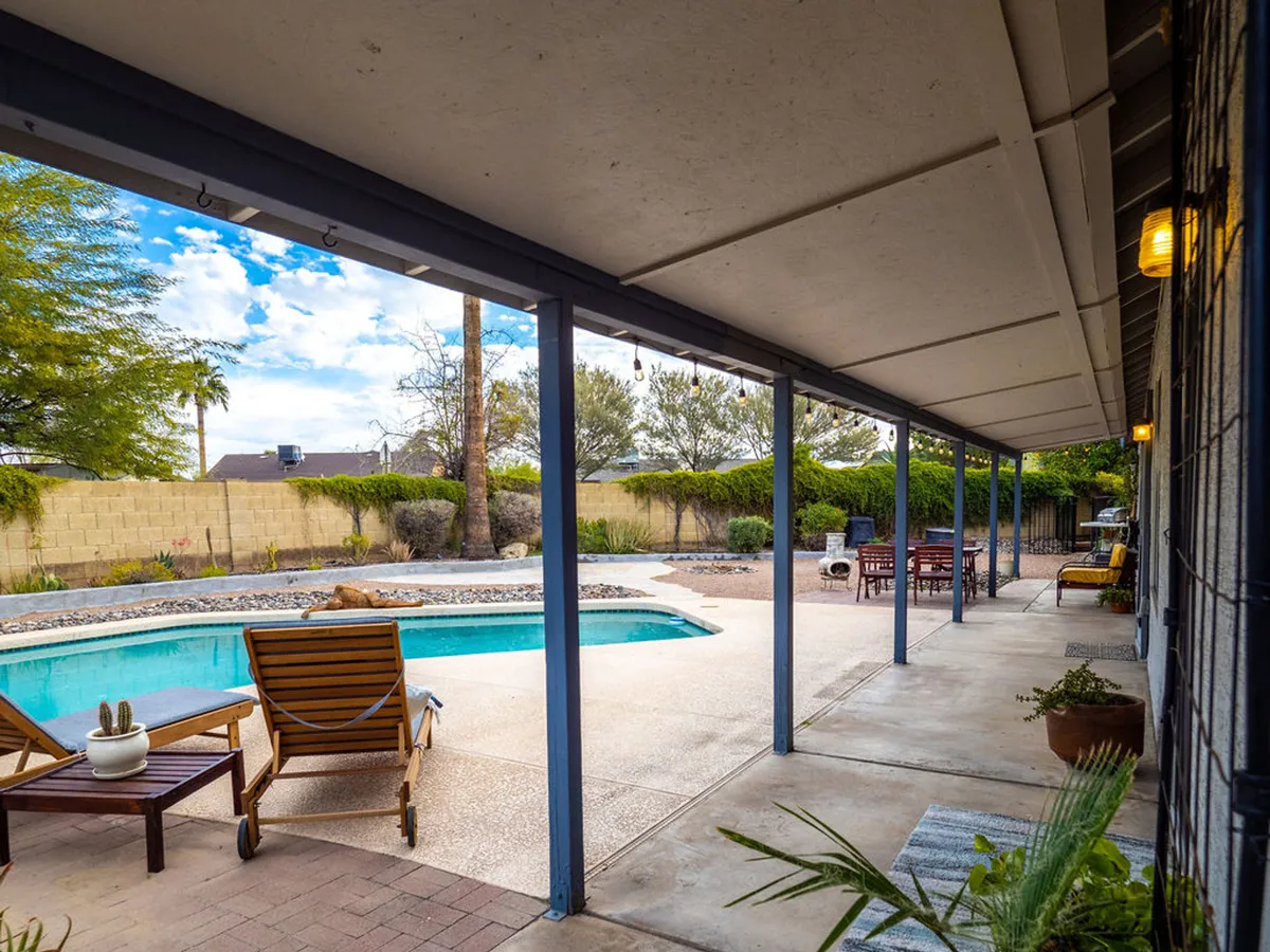 A relaxing scene featuring a tranquil swimming pool surrounded by lounge chairs and a well-maintained landscaped garden. The patio area is clearly visible, inviting both sunbathing and alfresco meals in a peaceful setting. The image is taken at a time of day that suggests either morning coffee or evening gatherings.